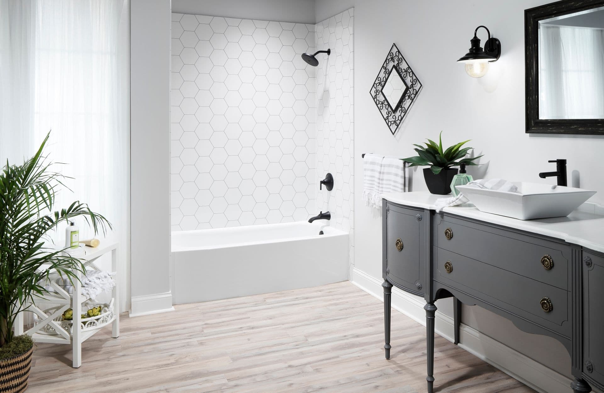 A white bathroom with a gray vanity and a combination shower bathtub with white hexagonal pattern walls and black fixtures.