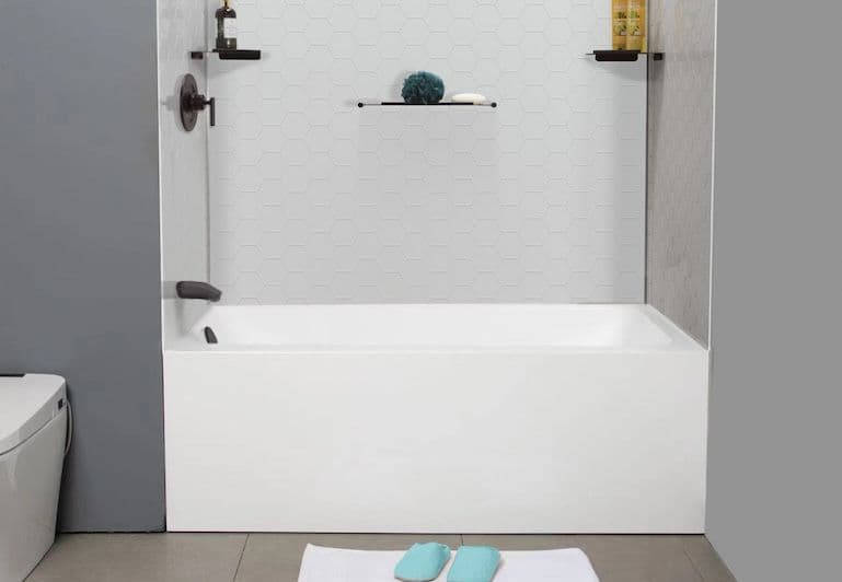 A white bathtub with black fixtures and white hexagonal patterned walls in a gray bathroom.