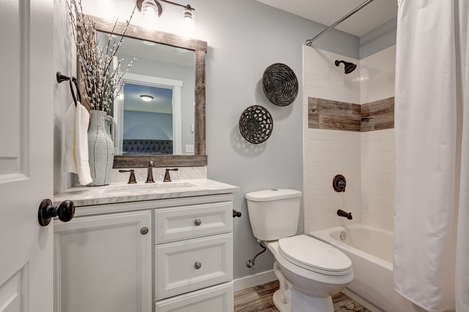 White bathroom with reclaimed wood details, vanity cabinet with marble counter top, and tub and shower combo accented with wood border.